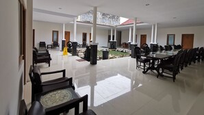 A spacious indoor area with multiple seating arrangements, including a long table and several chairs, a small garden area with a fountain, and a high ceiling with natural light. - Hotel Sumaryo (Yogyakarta)