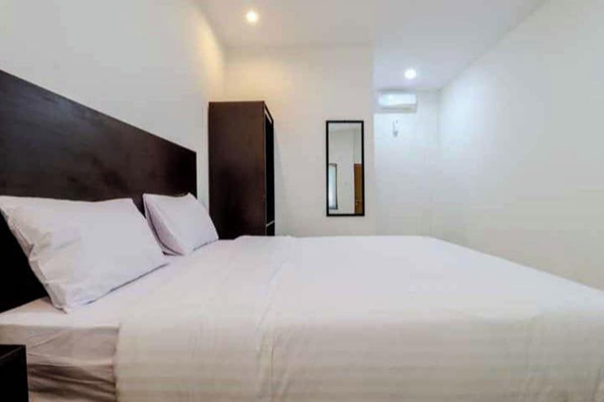 A hotel room with a large bed, a dark headboard, and a mirror on the wall.