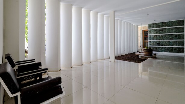 A spacious lobby with a row of white columns, a black seating area, and a green wall with a stone pattern. - Hotel Sumaryo (Yogyakarta)
