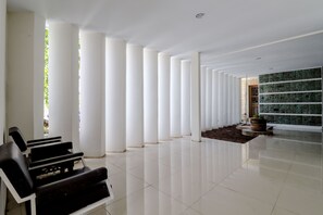 A spacious lobby with a row of white columns, a black seating area, and a green wall with a stone pattern. - Hotel Sumaryo (Yogyakarta)