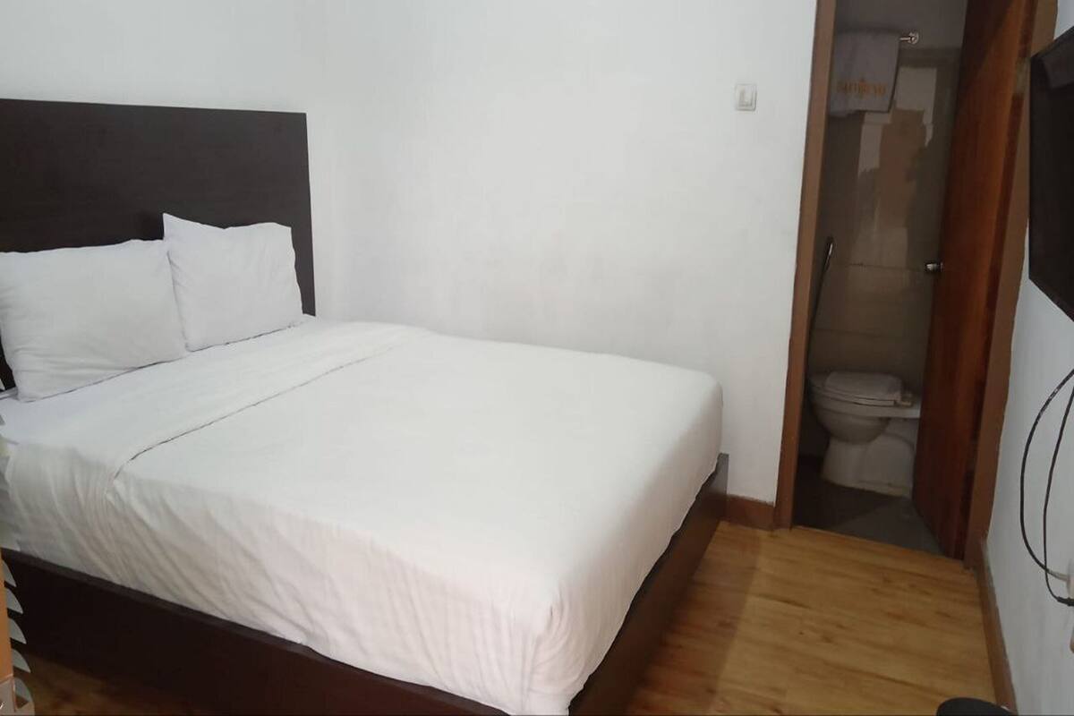 A bedroom with a bed, a wooden headboard, and a white wall.