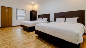 A hotel room with two beds, wooden flooring, a large window, and a door. - Hotel Sumaryo (Yogyakarta)