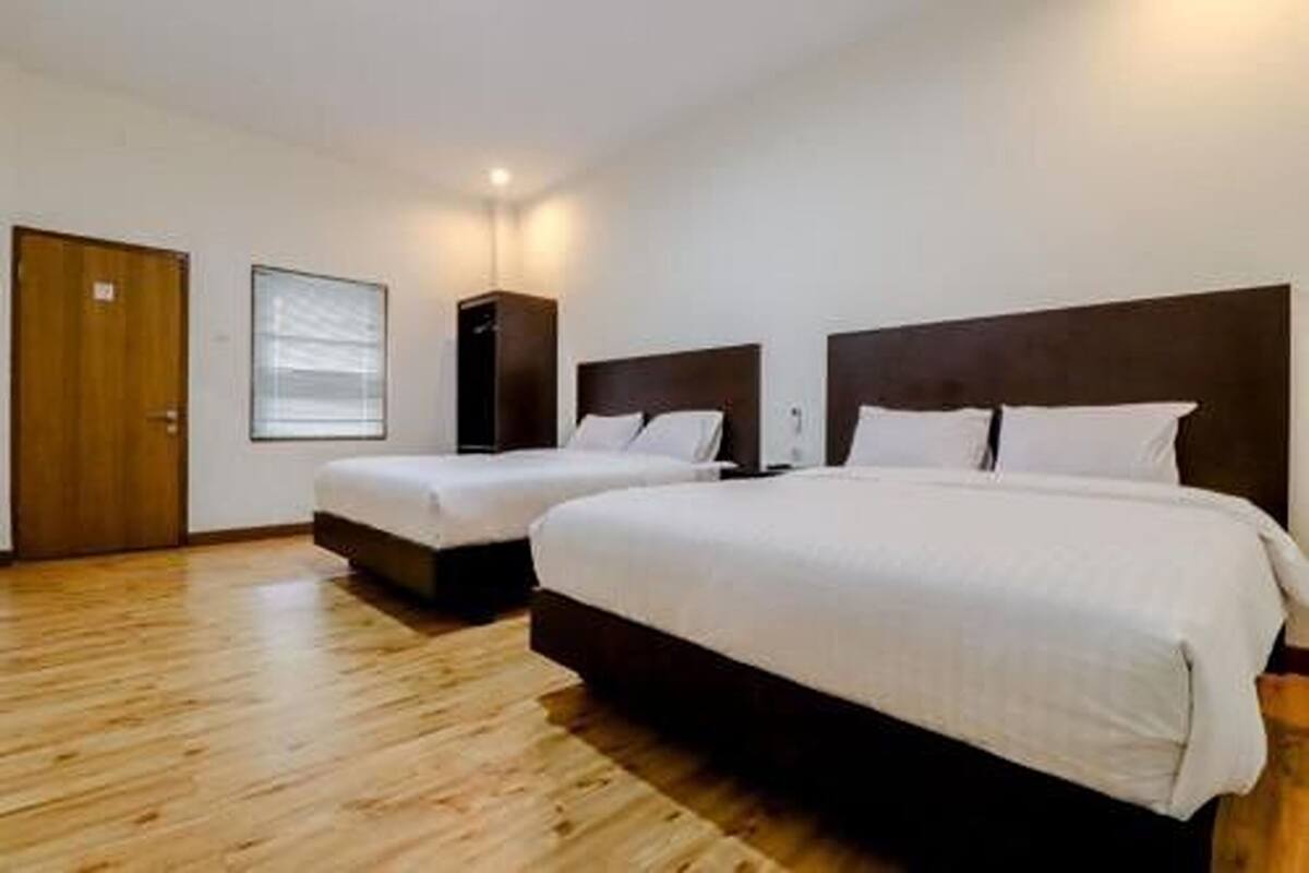 A hotel room with two beds, wooden flooring, a large window, and a door.