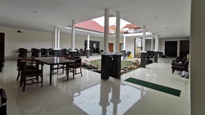 A spacious indoor area with a high ceiling, a central seating area with tables and chairs, and a view of a red-tiled roof through an open space. - Hotel Sumaryo (Yogyakarta)