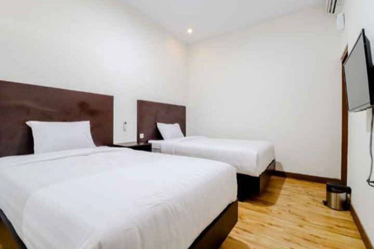 A hotel room with two beds, wooden flooring, and a TV mounted on the wall.