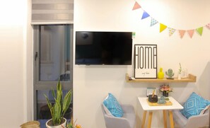 A modern living room with a flat-screen TV, a 'HOME' sign, a small table with a tray, and two chairs. - The Art - Bong Gio House (Ho Chi Minh City)