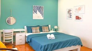 A bedroom with teal walls, a bed with a blue bedspread, two pillows, a bedside table with a lamp, a chair, and a mirror on the wall. - The Art - Bong Gio House (Ho Chi Minh City)