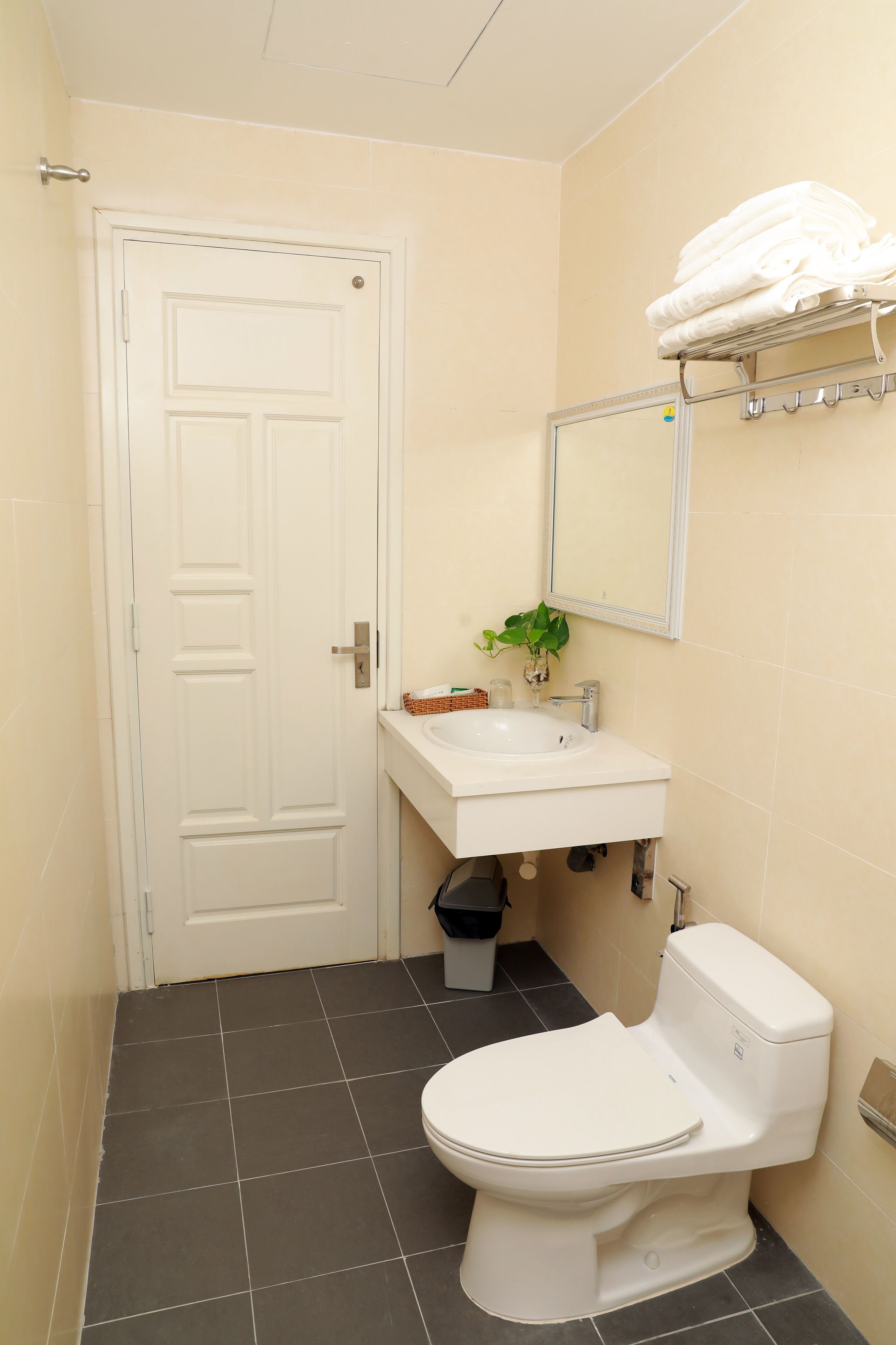 A bathroom with a white toilet, a sink, and a mirror above it. There is a towel rack with folded towels on it.