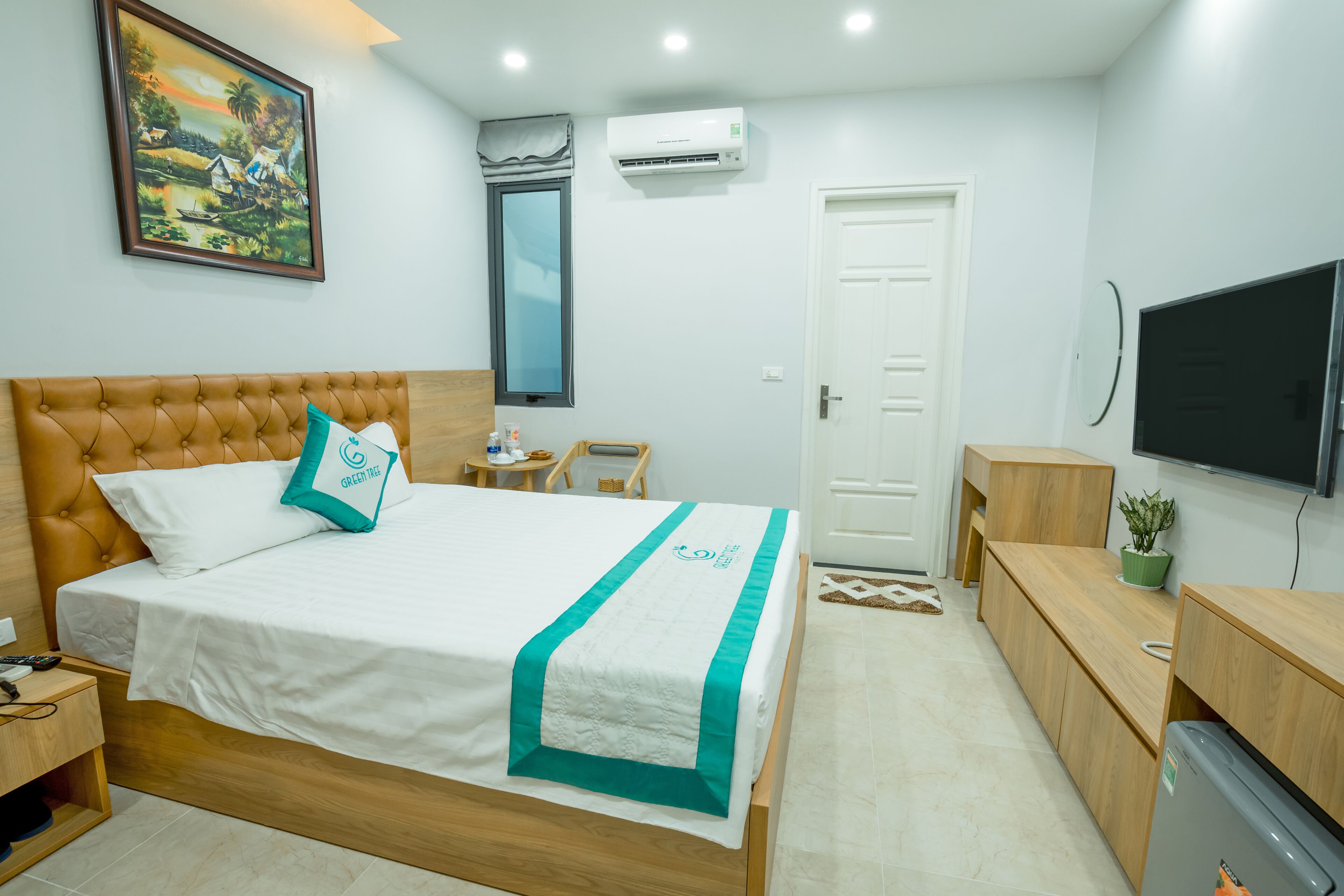 A neatly arranged bedroom with a bed, bedside table, TV, and a small desk area.