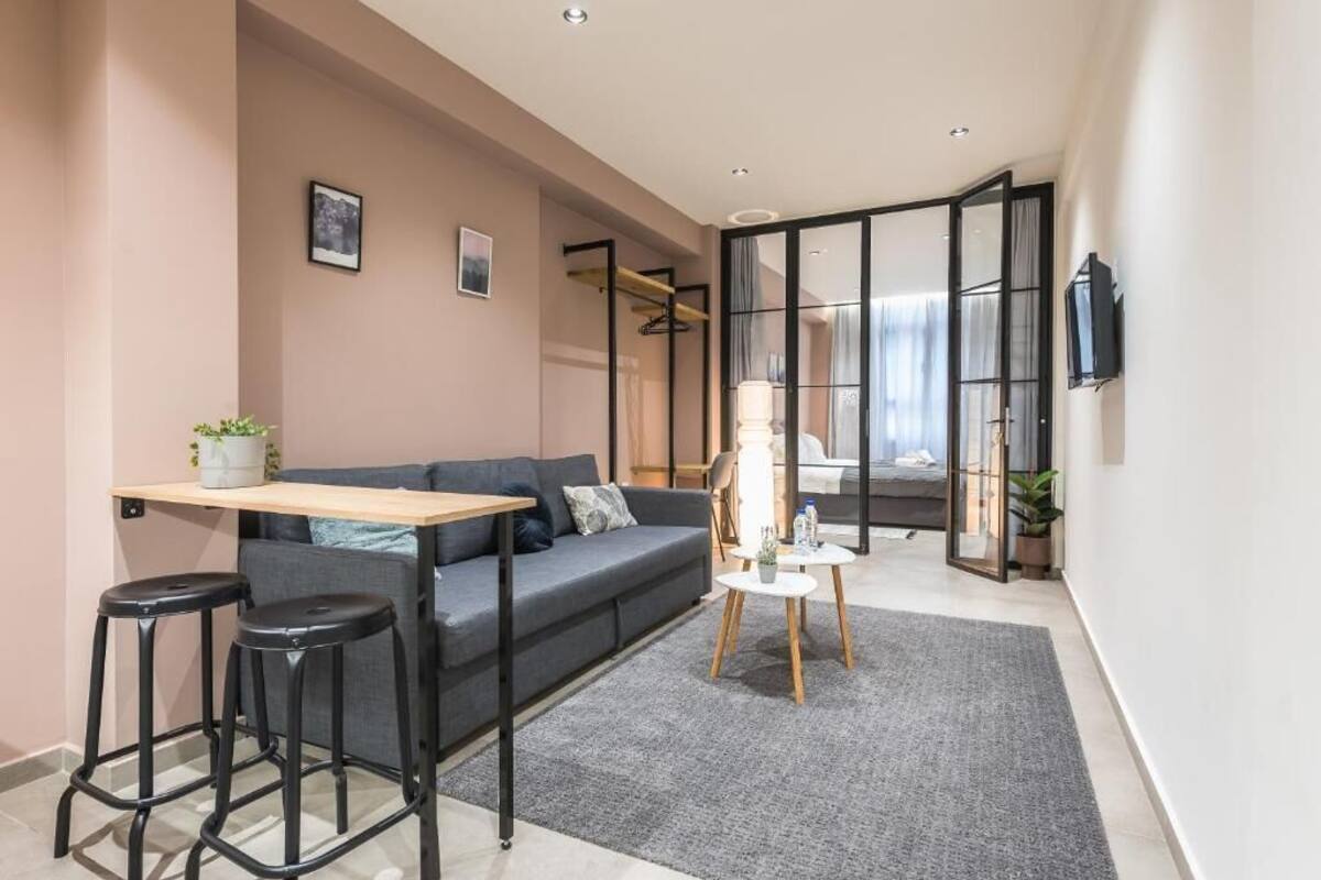 A modern living room with a sofa, two bar stools, a small table, and a TV mounted on the wall.
