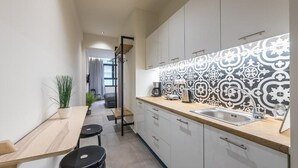 A modern kitchen with a wooden countertop, a sink, and patterned backsplash. There is a plant on the left and a bench with stools. - Filia Place (Athens)