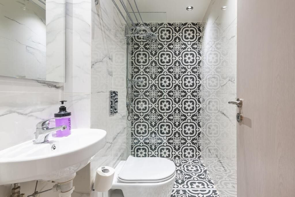 Een badkamer met een wit wastafelmeubel, een toilet en een douche met betegelde muren.