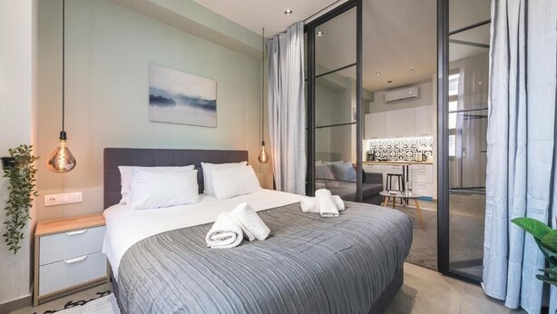 A modern hotel room with a large bed, a desk, and a view through a glass door. - Filia Place (Athens)