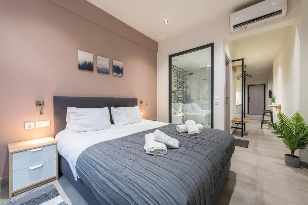 A modern hotel room with a large bed, bedside tables, a glass shower area, and a view of the hallway.