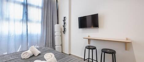 A hotel room with a bed, a TV mounted on the wall, a clock, and two bar stools.