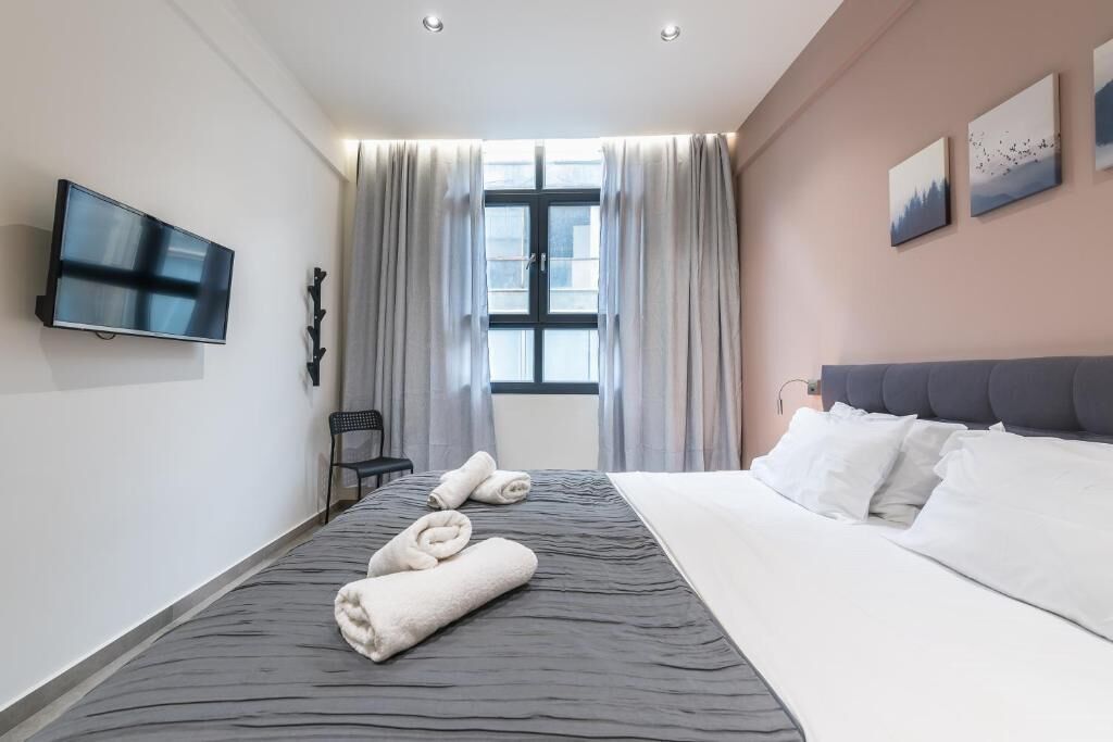 Una camera d'albergo con un letto grande, una TV a schermo piatto fissata al muro, una finestra con tende e opere d'arte appese al muro.