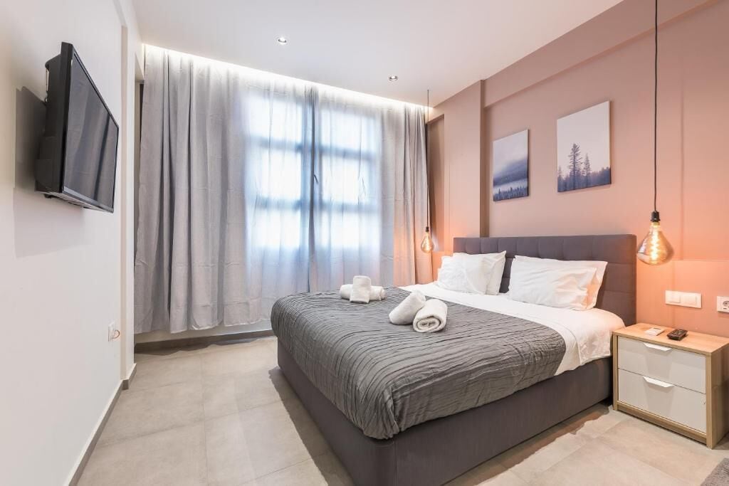 A modern bedroom with a large bed, a TV mounted on the wall, and a nightstand with a lamp.