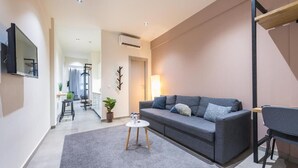 A modern living room with a grey sofa, a small white coffee table, and a TV mounted on the wall. - Filia Place (Athens)