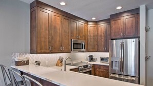 A modern kitchen with wooden cabinets, stainless steel appliances, and a white countertop. - Solitude Mountain Slopeside Ski Condo w/ Hot Tub! (Brighton)