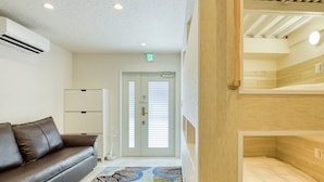 A hotel room with a brown leather sofa, a wooden bunk bed, a white door with blinds, and a ceiling with recessed lighting.