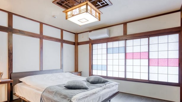 A traditional Japanese-style bedroom with tatami flooring, a low wooden bed, and a shoji screen window.