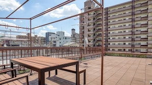 A rooftop terrace with a wooden table and benches, overlooking a cityscape with residential buildings.