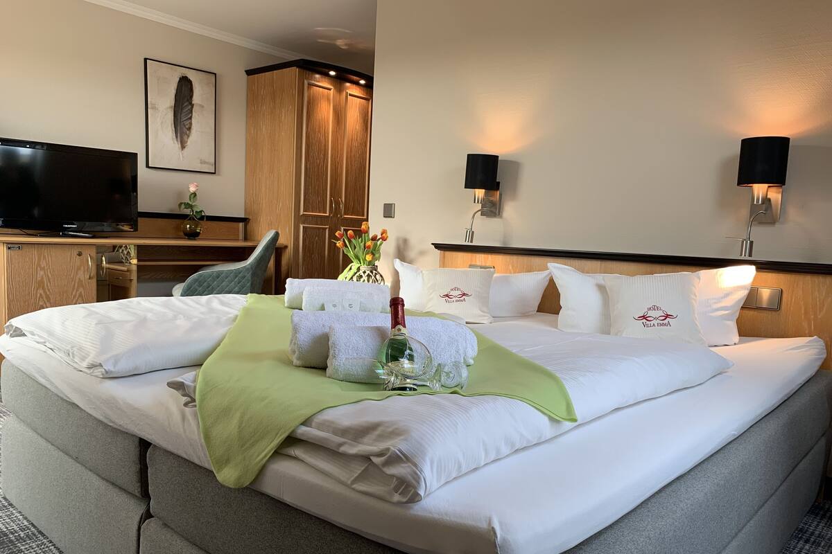 A hotel room with a large bed, a flat-screen TV, wooden wardrobe, and two wall-mounted lamps.