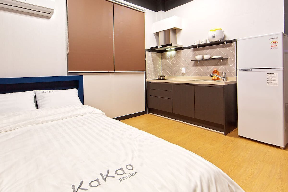 A compact hotel room with a bed, a kitchenette, and a small bathroom.
