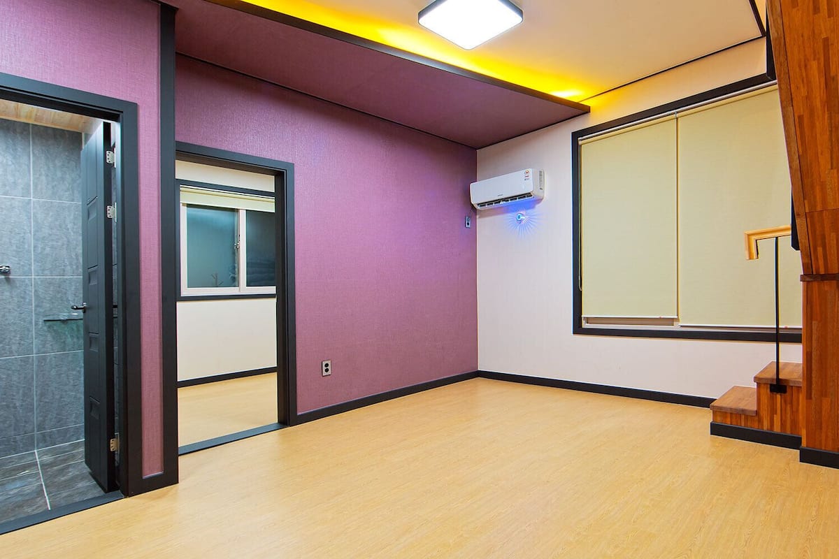 A modern hotel room with a purple wall, a wooden staircase, and a large window.