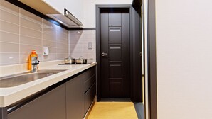 A compact kitchen with a dark door, a countertop with a sink, and two pots on the stove. - Kakao Pension (Boryeong)