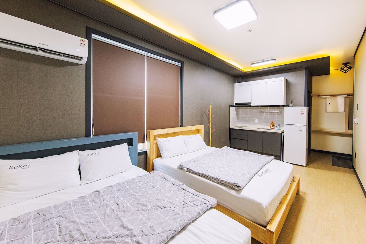 A hotel room with two beds, a kitchenette, a refrigerator, and an air conditioning unit.