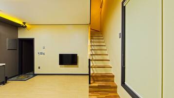 Un couloir d’hôtel moderne avec un escalier en bois, un téléviseur à écran plat fixé au mur et une porte dotée d’un interrupteur.