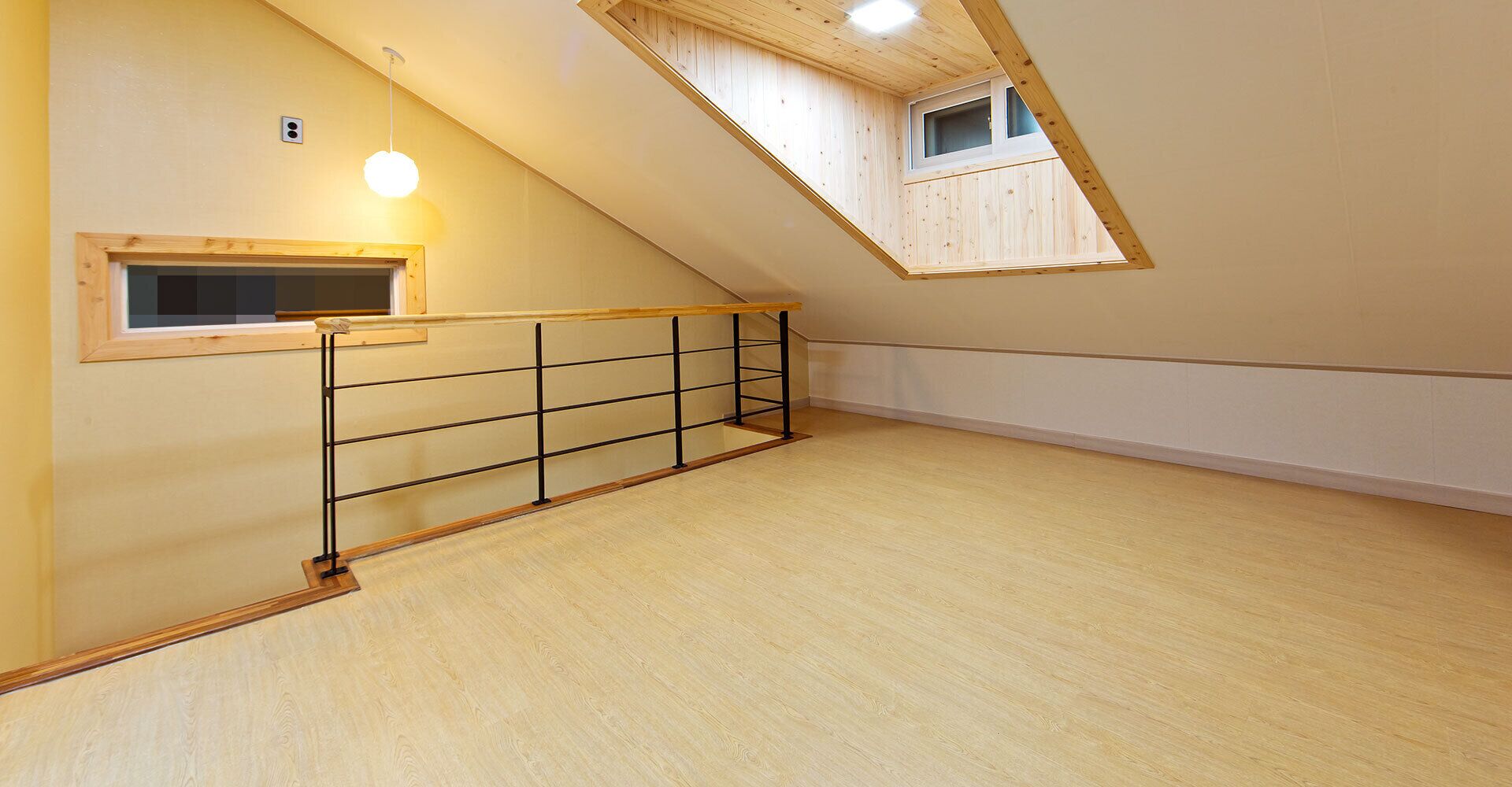 Een kamer met een houten vloer, een houten trap, een metalen leuning en een dakraam.
