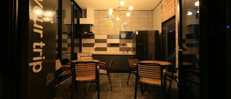 A modern restaurant with a checkered wall pattern, a central dining area with wooden chairs, and a visible kitchen counter.