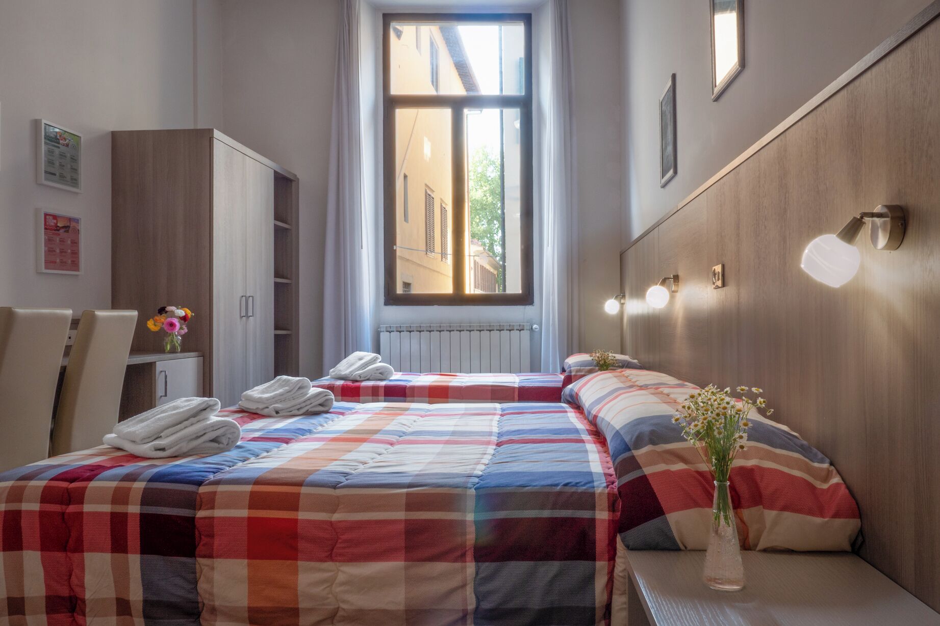 Una habitación de hotel con dos camas, una ventana, un armario y un escritorio con una silla.