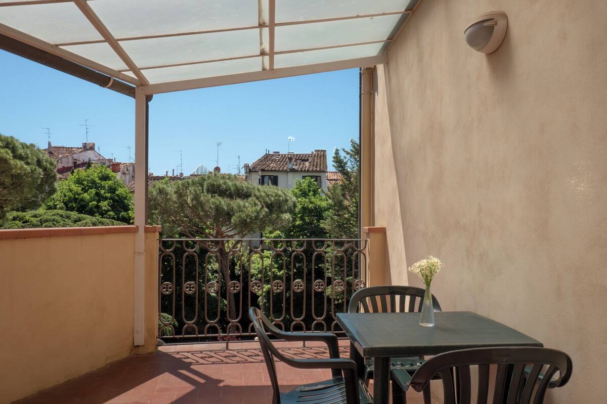 Ein Balkon mit Tisch und Stühlen, eine Glastür und Blick auf Gebäude und Bäume.