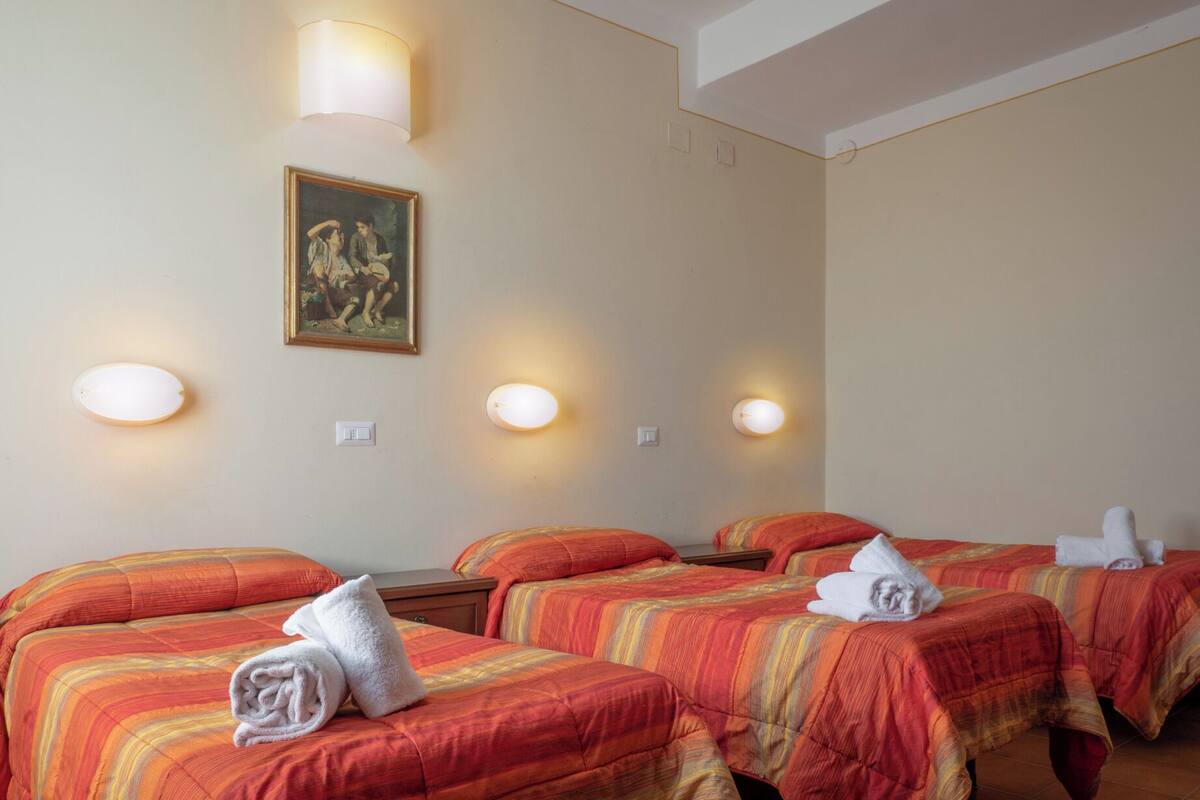 Ein Hotelzimmer mit vier Betten, jedes mit einem Handtuch, einem Bild an der Wand und Wandleuchten.