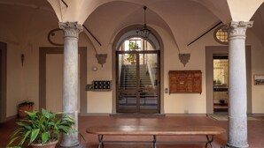 A covered entrance with a bench, columns, a staircase, and a wooden cabinet. - Foresteria Valdese di Firenze - Casa per Ferie (Florence)