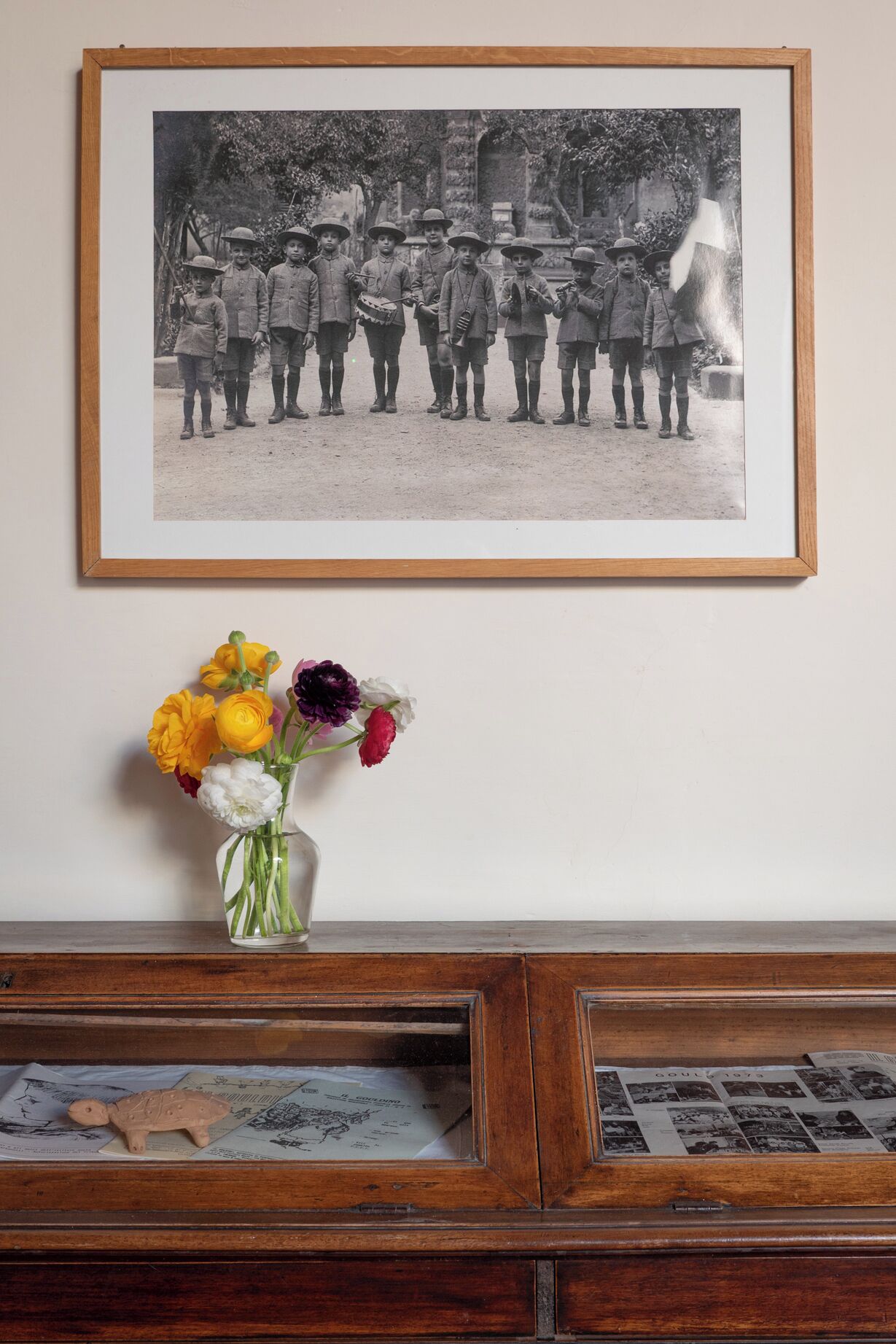 A framed historical photograph above a wooden cabinet with a vase of flowers.