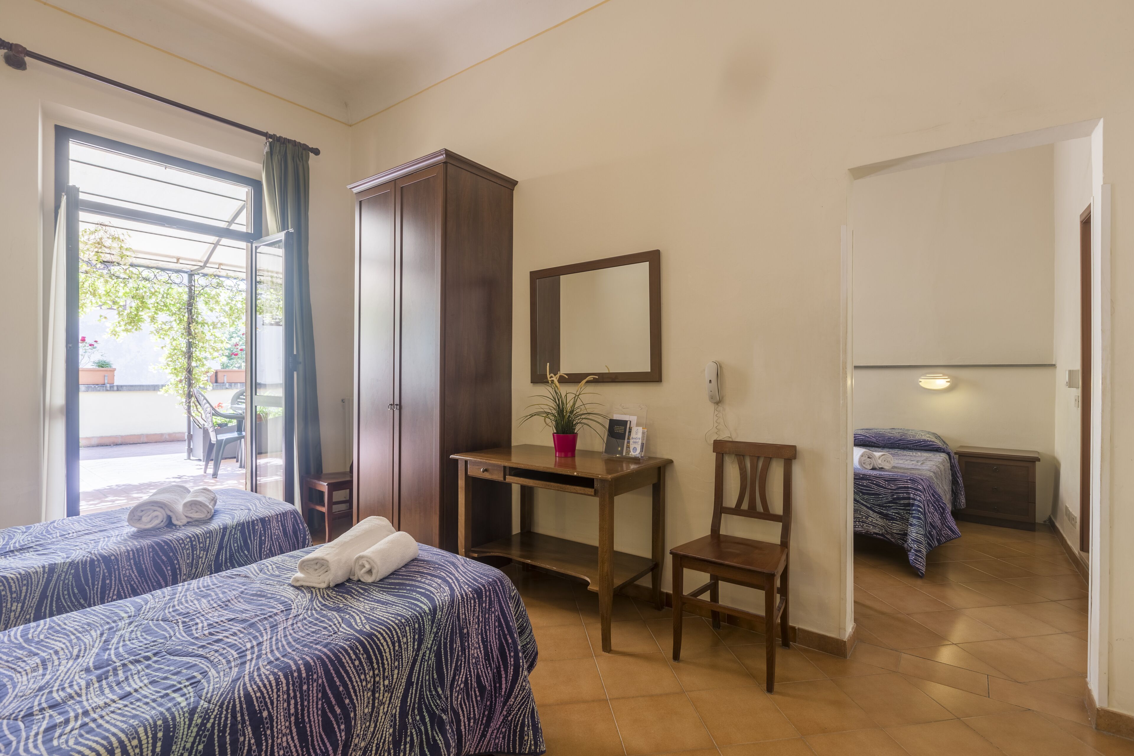 Habitación de hotel con dos camas, un escritorio, una silla, un armario y una ventana con cortinas.