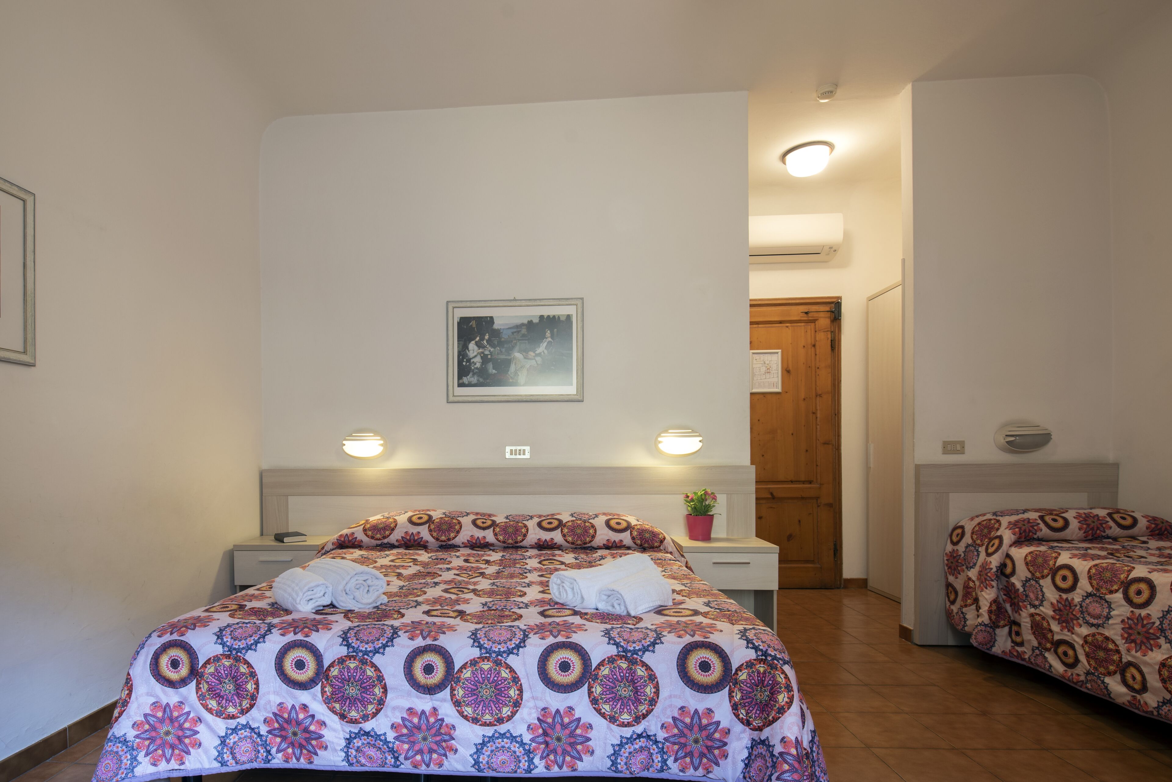 A bedroom with a bed, bedside tables, a wall-mounted picture, and a door.