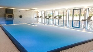Una piscina interior amb parets de vidre transparent, un paviment de rajoles i unes quantes gandules.
