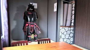 A room with a wooden table and chairs, a decorative samurai statue, and a patterned wall. - Nakagawanisi Samurai House3 (Osaka)