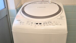 A front-loading washing machine with a control panel, a power cord, and a detergent dispenser on a wall-mounted shelf. - Nakagawanisi Samurai House3 (Osaka)