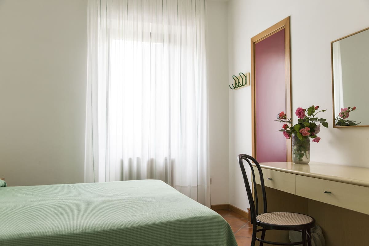 A room with a bed, a desk, a chair, a mirror, and a window with curtains.