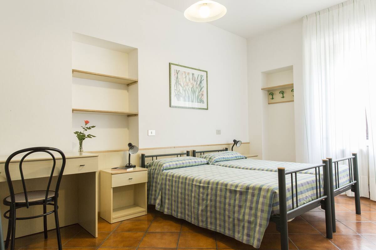A bedroom with a bed, a desk, a chair, and a wall-mounted shelf.