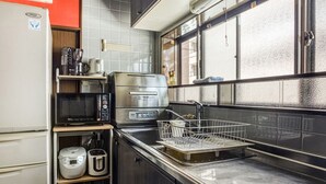 A compact kitchen with a microwave, toaster, and kettle on a countertop, a sink with a dish rack, and a refrigerator. - Ajiro Sakura House4 (Higashi-osaka)