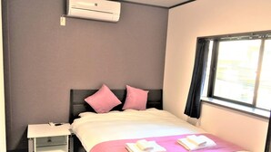 A hotel room with a bed, a nightstand, an air conditioner, and a window. - Ajiro Sakura House4 (Higashi-osaka)