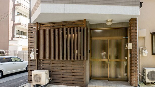 A building entrance with a wooden gate, air conditioning units, and a potted plant. - Ajiro Sakura House4 (Higashi-osaka)