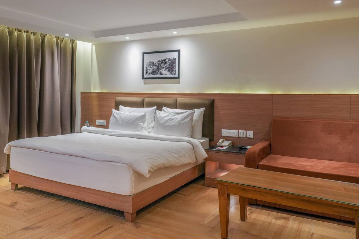 Une chambre d’hôtel avec un grand lit, une tête de lit en bois, une table de chevet avec un téléphone, une petite table et un canapé.